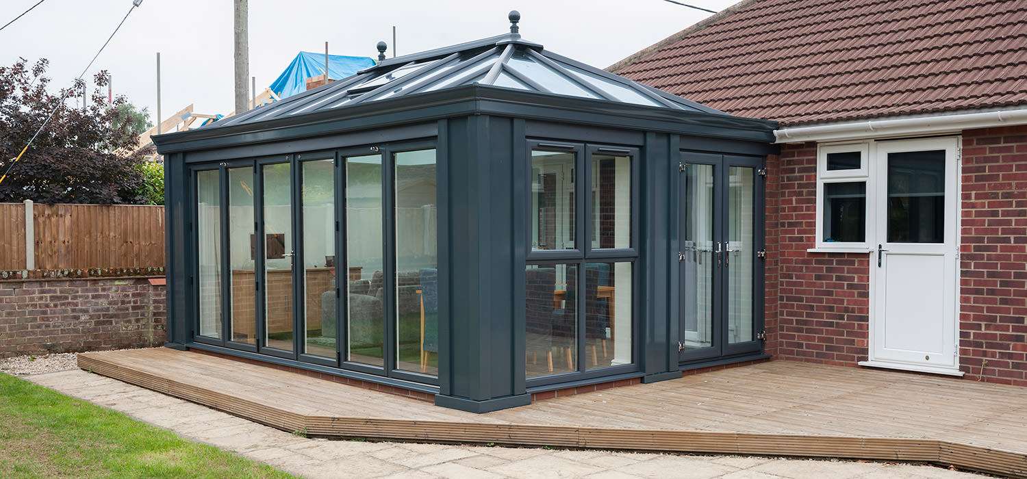 A contemporary anthracite-grey conservatory with a glass roof on a decked patio