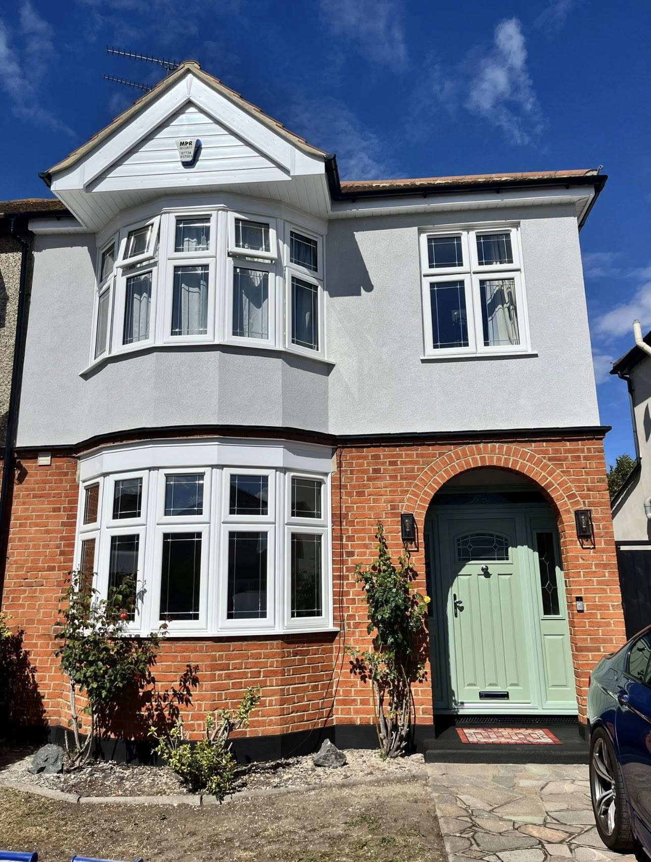 Two-storey white uPVC bay windows on a render and red brick semi-detached home