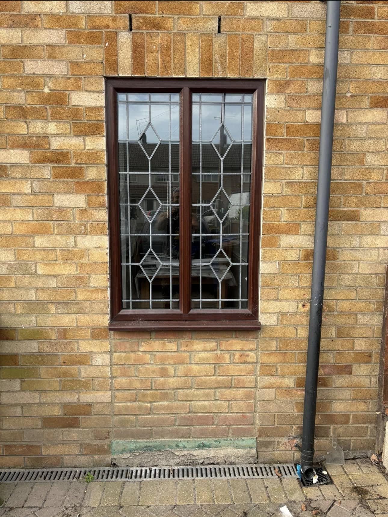 Rosewood-effect heritage uPVC window with leaded diamond glazing on a brick wall