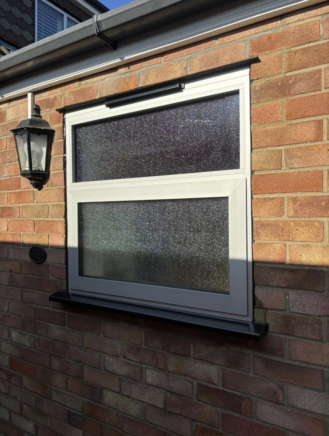Silver anodised aluminium window with obscure glass and black sill on a brick wall